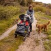 Szczęśliwa mama z dzieckiem w wózku rehabilitacyjnym Comfort oraz psem na spacerze